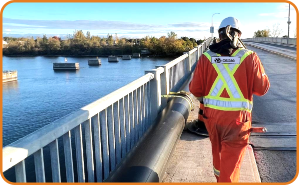 Primapipe technician overseeing large-diameter pipeline installation across a bridge over a river.