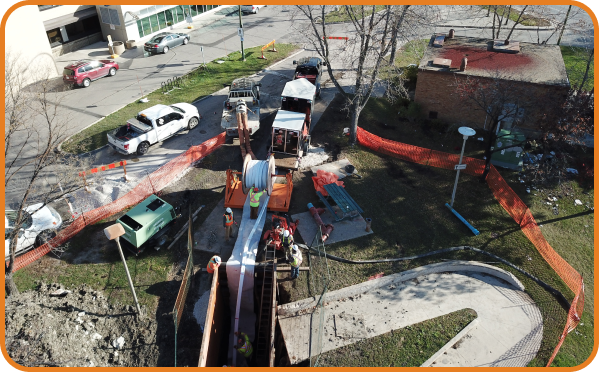 Aerial view of Primapipe crew performing urban water pipeline rehabilitation using trenchless technology near a commercial facility.